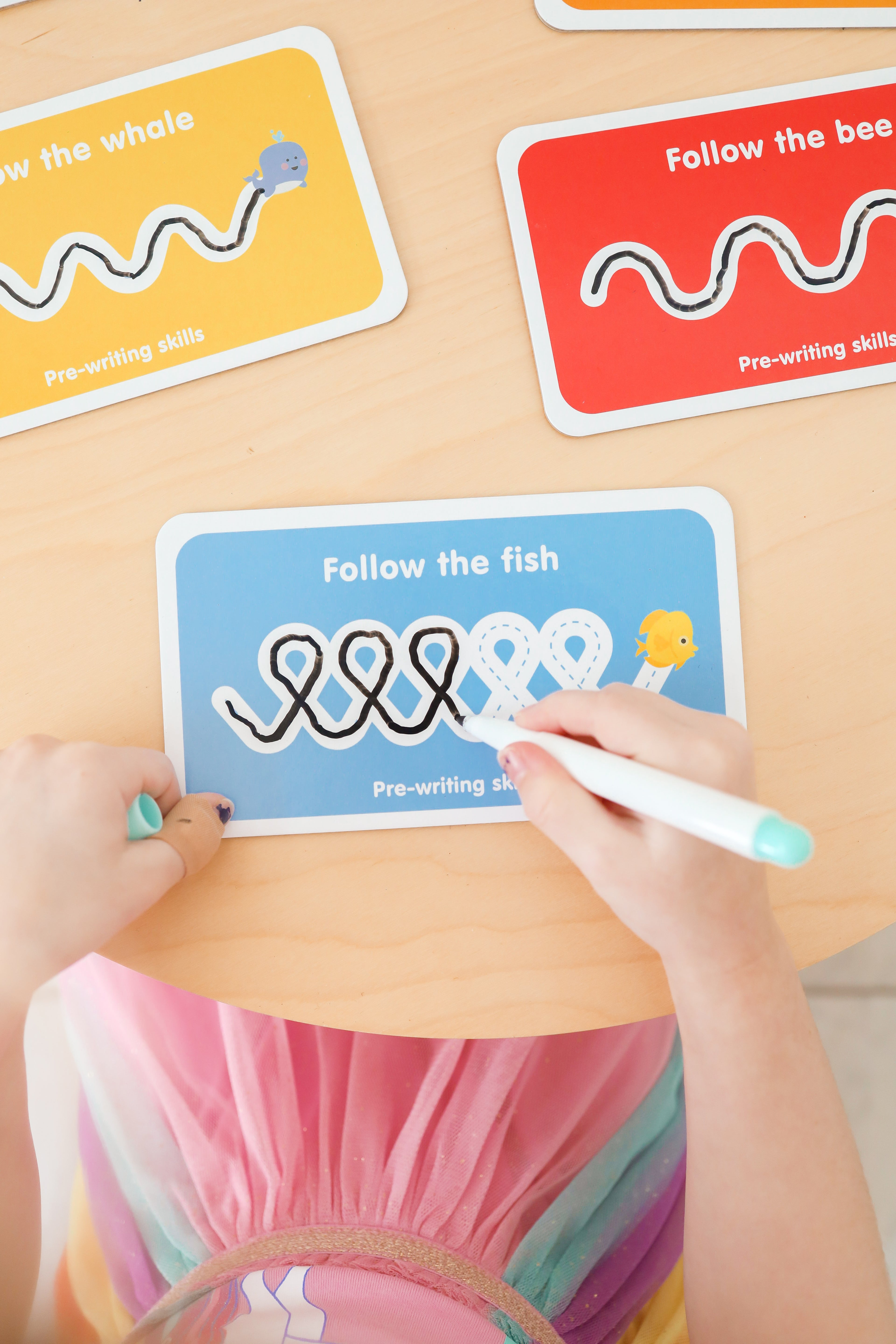 Child using a marker to follow pre-printed lines on educational cards with cartoon animals.
